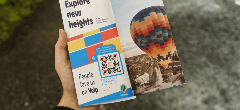 A hand holding a brochure for a hot air balloon business featuring a Yelp QR Code.